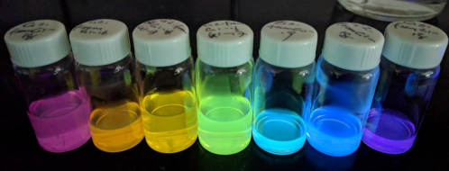 a set of vials containing a rainbow of carbon dots glowing with bright colors 