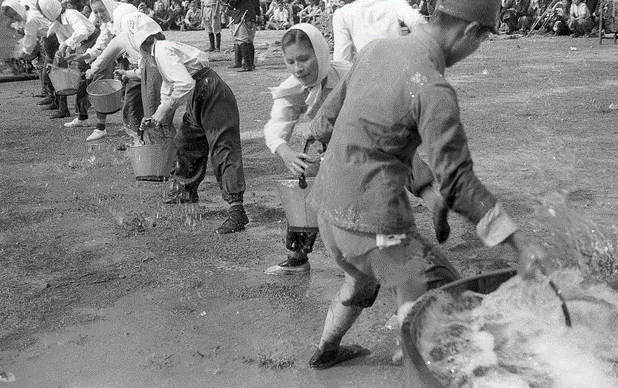 A black and white picture with people passing buckets of water down a line. 