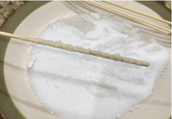 photo of a plate of sugar with wooden stick that has been rolled in the sugar and now has crystals stuck all around it