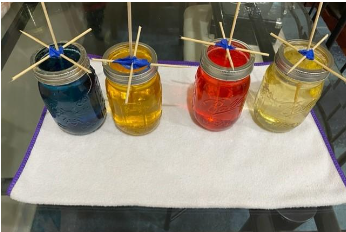 photo of glass jars full of colorful liquid and sticks rigged with tape and cross-pieces to stand vertically in the liquid