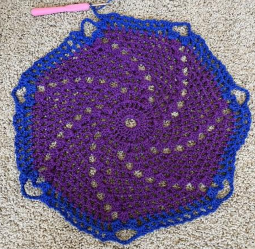 the same purple spiral crochet project showing further progress with a blue layer around the outside