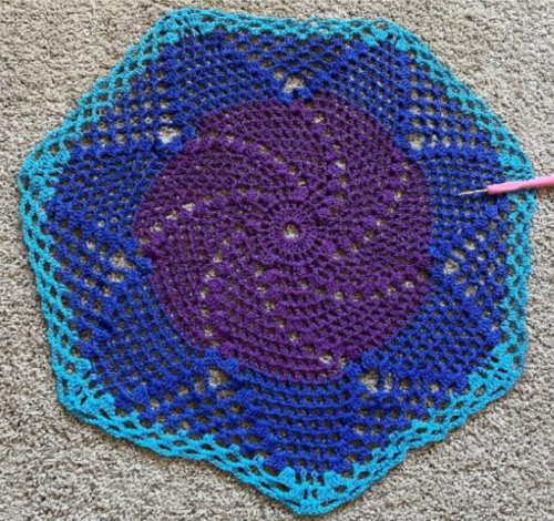 finished crochet doily project showing the spiral pattern comprising purple at the center, surrounded by a dark blue layer, and a light blue layer around the outside